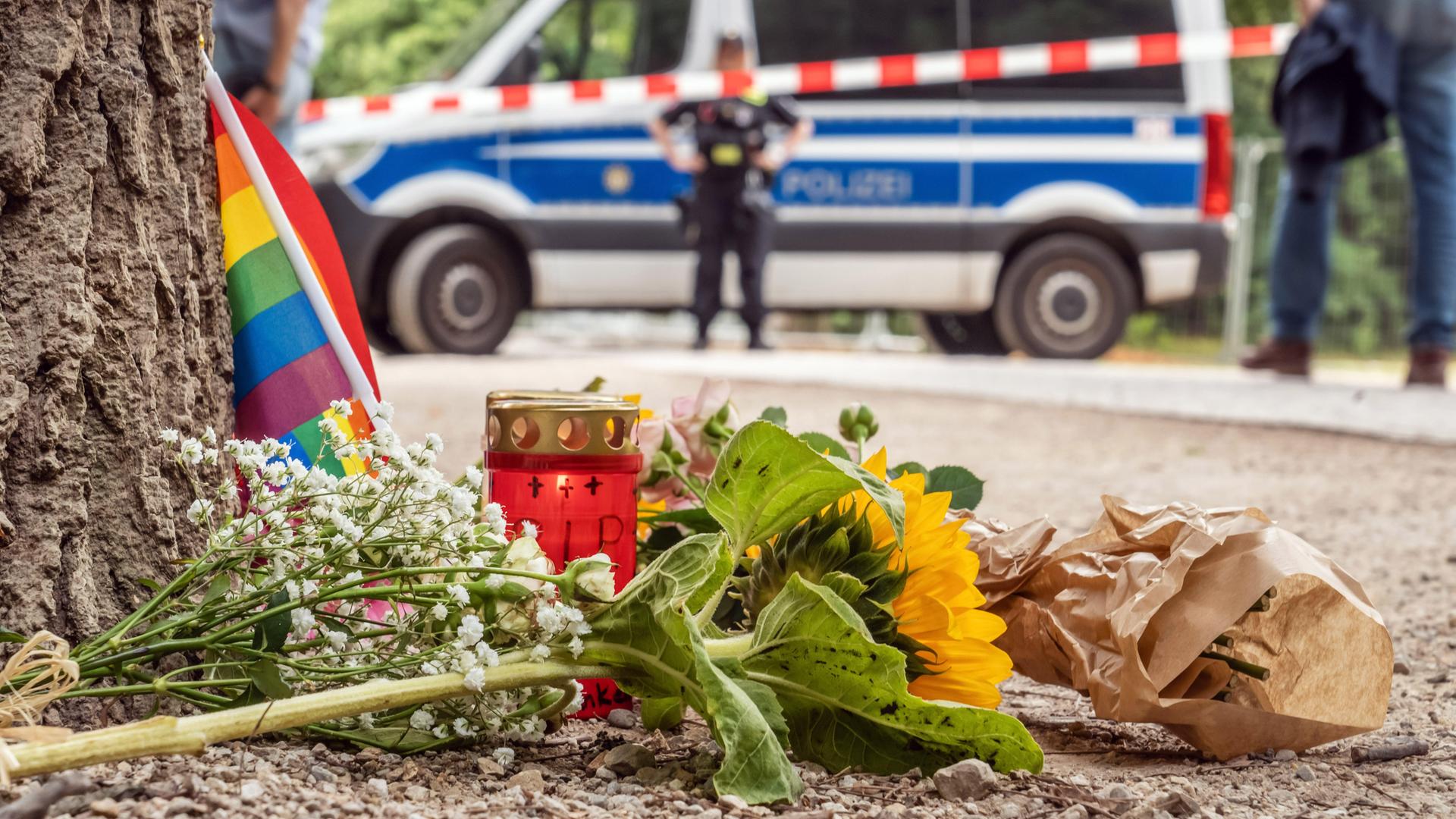 Passanten haben 80 Meter vom Tatort des CSD-Anschlags eine Regenbogenfahne, ein Grablicht und Sonnenblumen niedergelegt. Im Hintergrund ist ein Polizeibus zu erkennen. Passanten haben 80 Meter vom Tatort des CSD-Anschlags eine Regenbogenfahne, ein Grablicht und Sonnenblumen niedergelegt. Im Hintergrund ist ein Polizeibus zu erkennen.