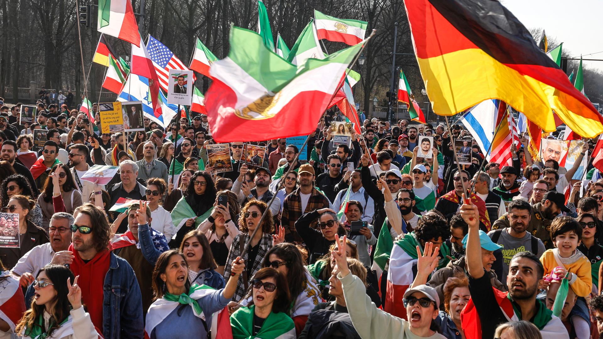 Das Foto zeigt eine Menschenmenge, die iranische, deutsche, US-amerikanische und israelische Flaggen schwenkt und gegen das iranische Regime protestiert. Die Demonstration fand am 7. März 2026 in Berlin statt.