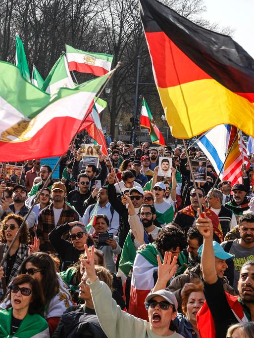 Das Foto zeigt eine Menschenmenge, die iranische, deutsche, US-amerikanische und israelische Flaggen schwenkt und gegen das iranische Regime protestiert. Die Demonstration fand am 7. März 2026 in Berlin statt.
