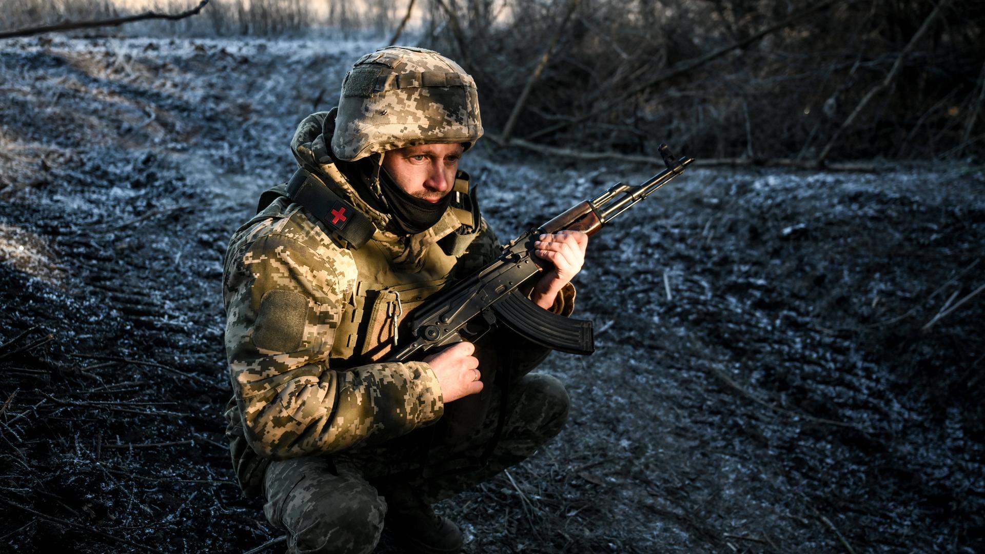 Ein Soldat hockt auf eisigem Boden und hält ein Gewehr.