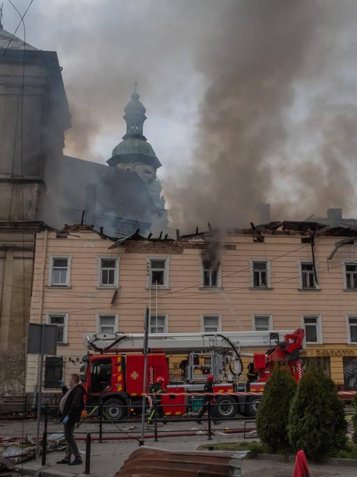 Rauch steht über einer alten Kirche. Neben der Kirche ist ein weiteres Gebäude, das auch beschädigt ist.