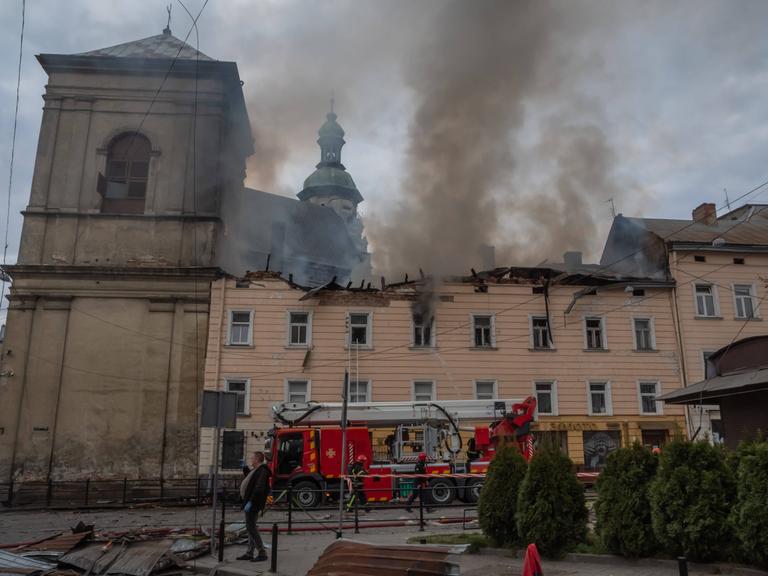 Rauch steht über einer alten Kirche. Neben der Kirche ist ein weiteres Gebäude, das auch beschädigt ist.