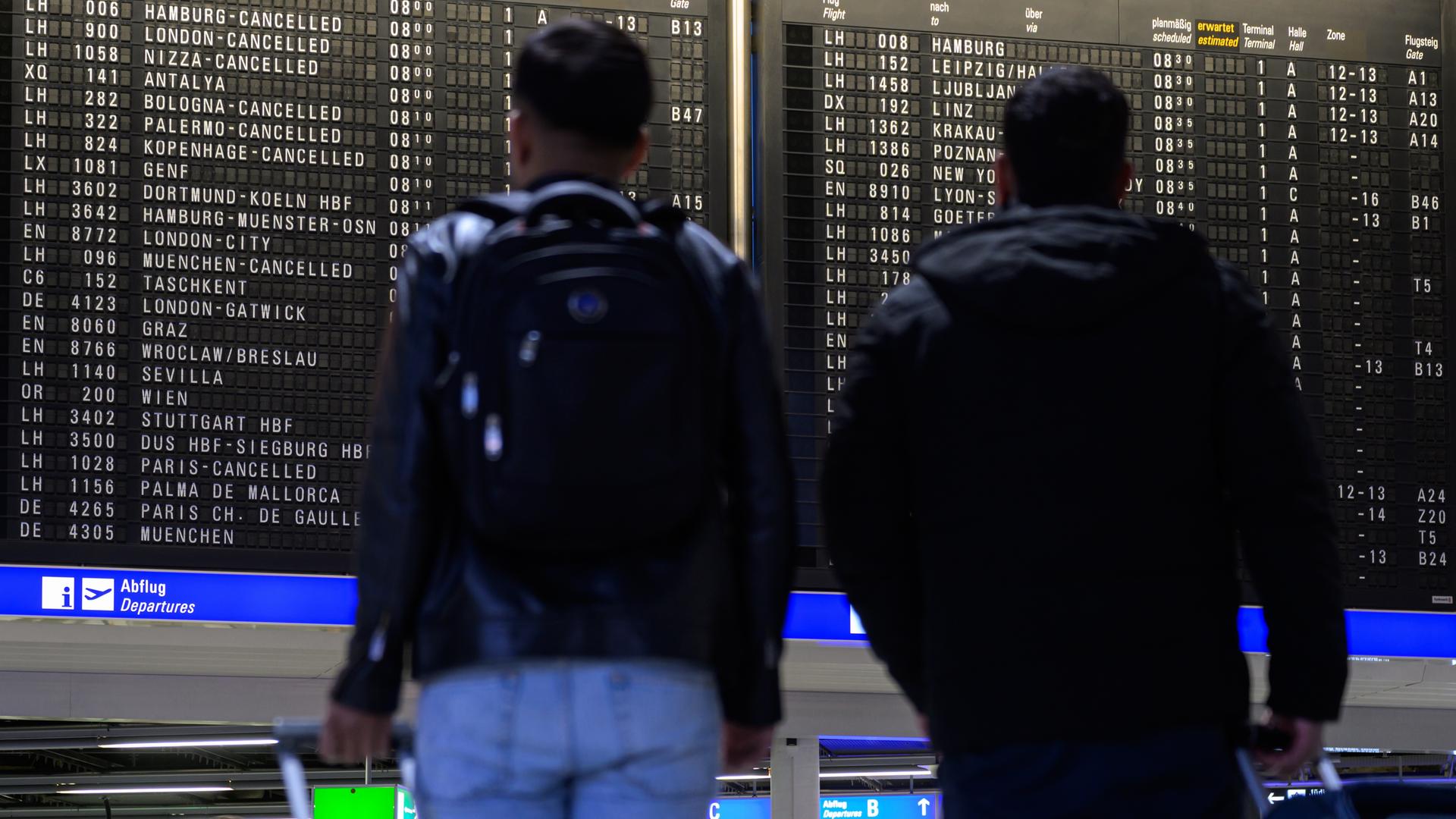 Menschen stehen vor einer Anzeigetafel mit gestrichenen Flügen der Lufthansa am Frankfurter Flughafen.