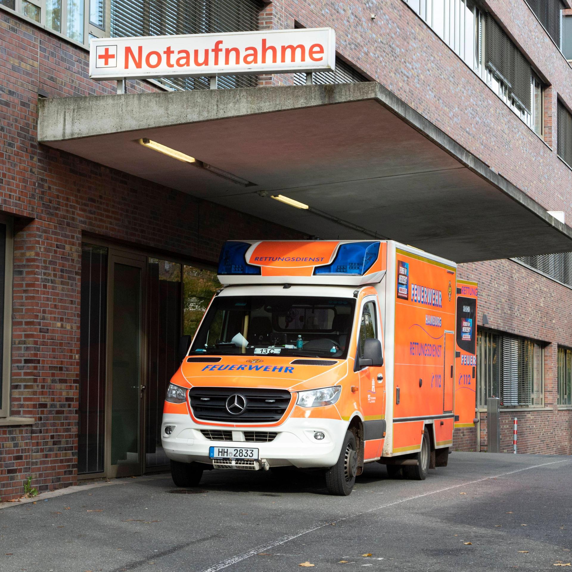 Ein Krankenwagen steht vor einem Krankenhaus. An dem backsteinernen Gebäude ist ein Schriftzug mit dem Wort "Notaufnahme" befestigt.