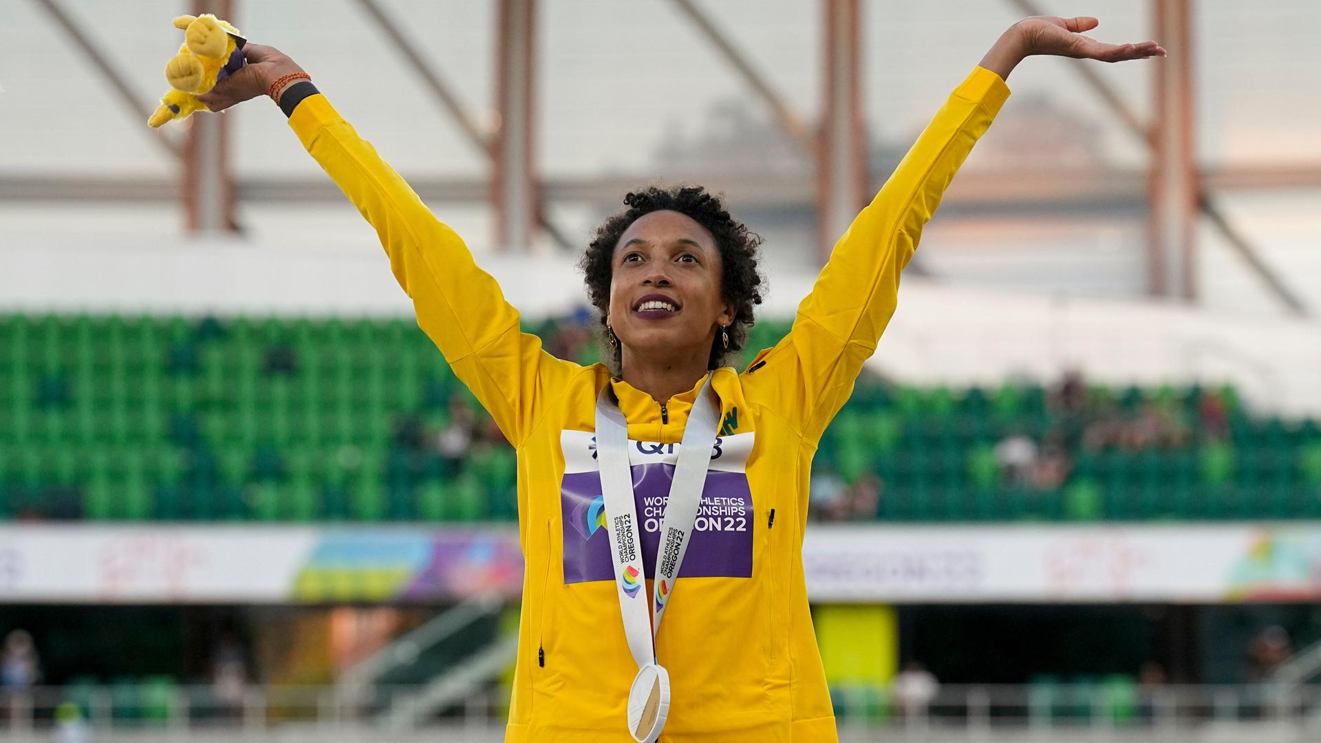 Die Weitspringerin Malaika Mihambo steht im Stadion in Oregon und reckt beide Arme in die Höhe. Um den Hals trägt sie ihre Goldmedaille.