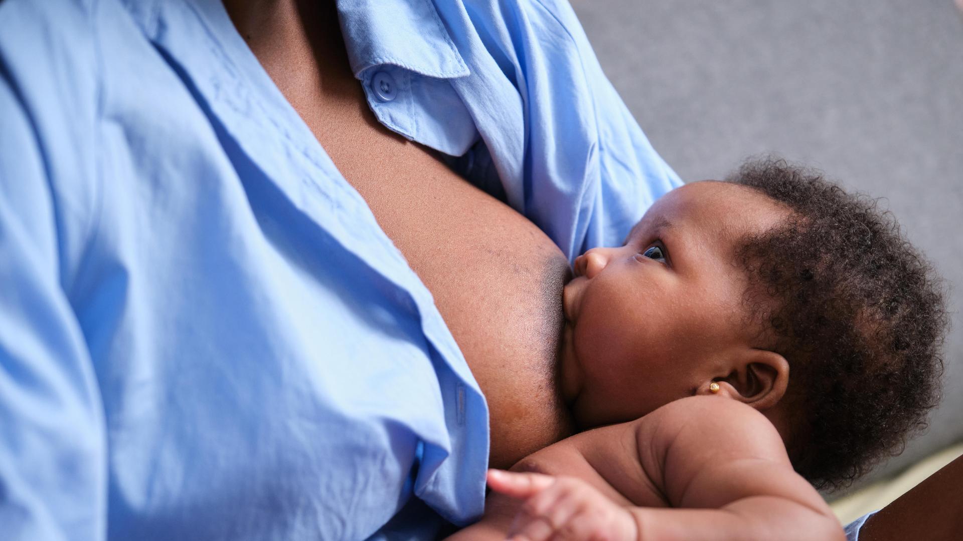 Ein Baby liegt an der Brust der Mutter und trinkt. Es schaut hoch zum Gesicht der Mutter.