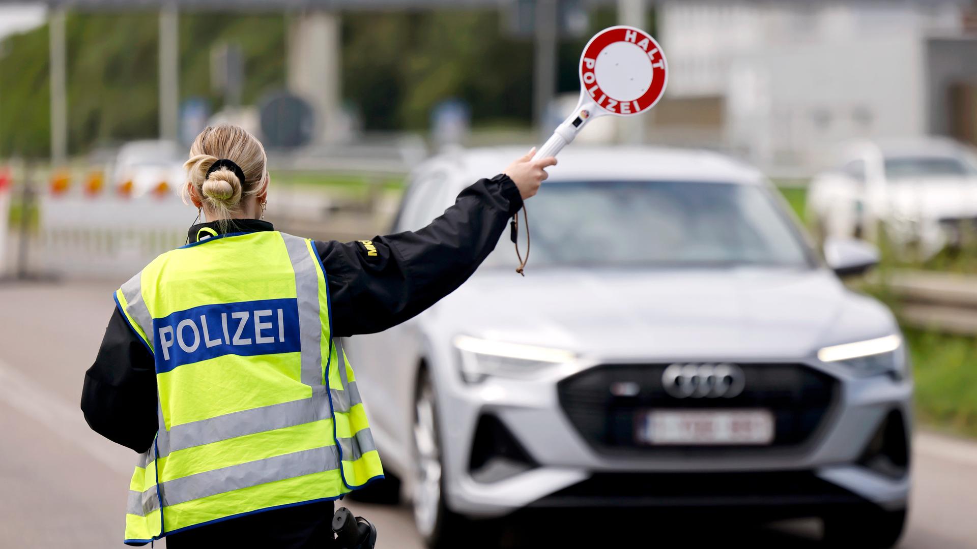 Das Bild zeigt eine Bundespolizistin, die einen silberfarbenen PKW mit einer Signalkelle stoppt. 