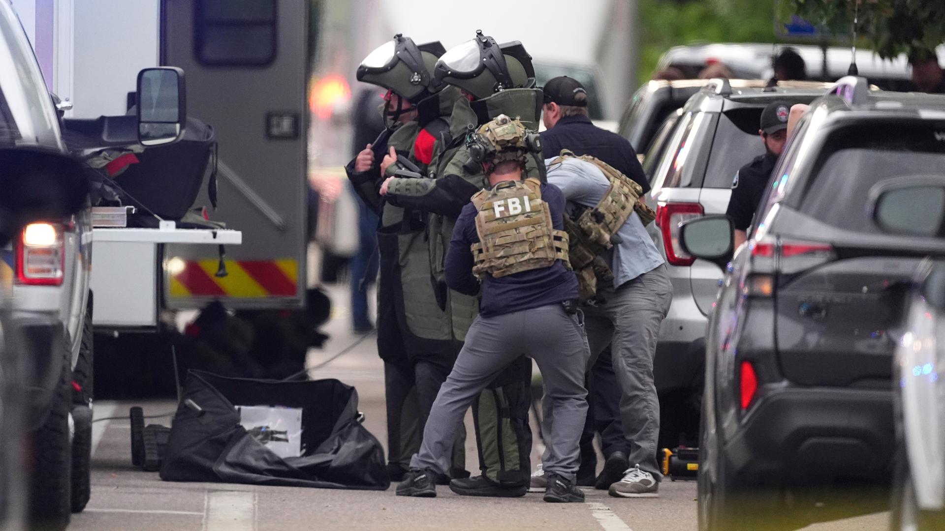 Ermittler stehen zwischen Einsatzfahrzeugen und ziehen sich Schutzkleidung an. Ermittler stehen zwischen Einsatzfahrzeugen und ziehen sich Schutzkleidung an.