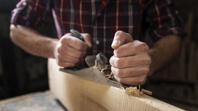 Eine Person bearbeitet in einer Holzwerkstatt mit einem Hobel ein Stück Holz.