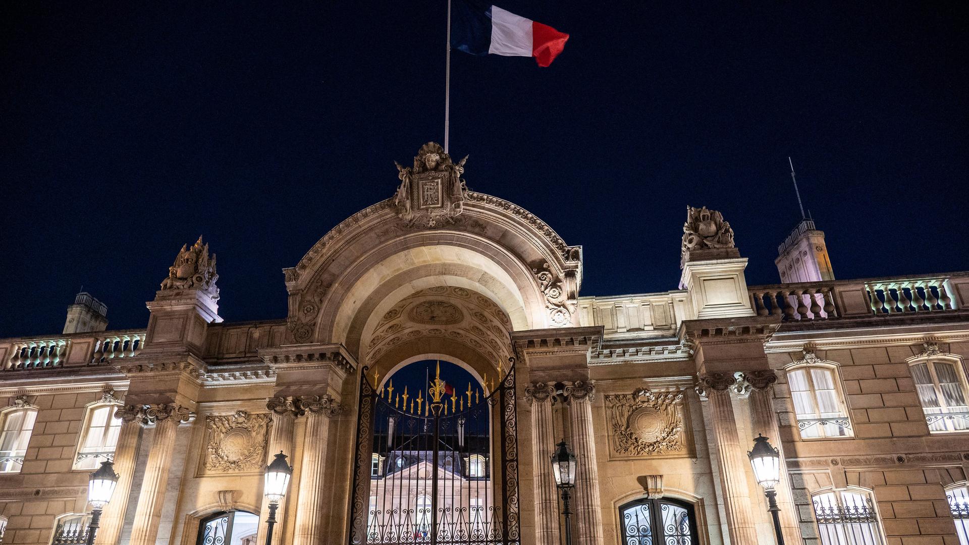 Über dem erleuchteten Elysee-Palast in Paris weht in der Dunkelheit eine Frankreich-Fahne.