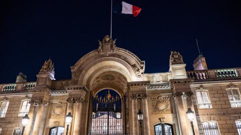 Über dem erleuchteten Elysee-Palast in Paris weht in der Dunkelheit eine Frankreich-Fahne.