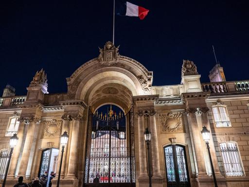 Über dem erleuchteten Elysee-Palast in Paris weht in der Dunkelheit eine Frankreich-Fahne.