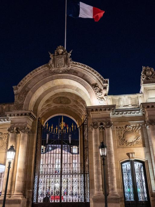 Über dem erleuchteten Elysee-Palast in Paris weht in der Dunkelheit eine Frankreich-Fahne.