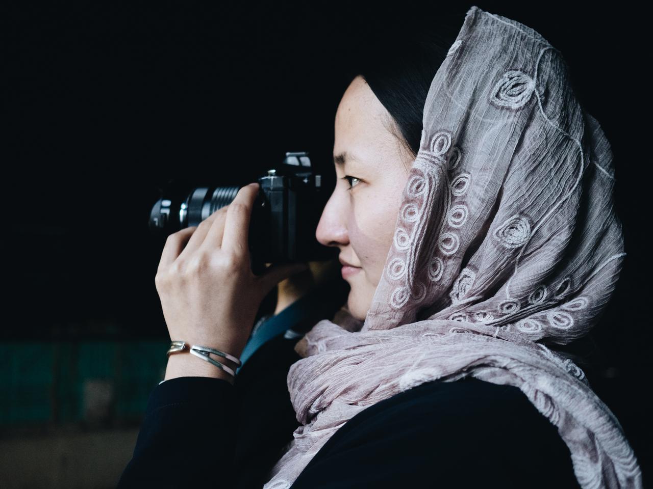 Eine junge Frau mit Kopftuch schaut durch eine Kamera.