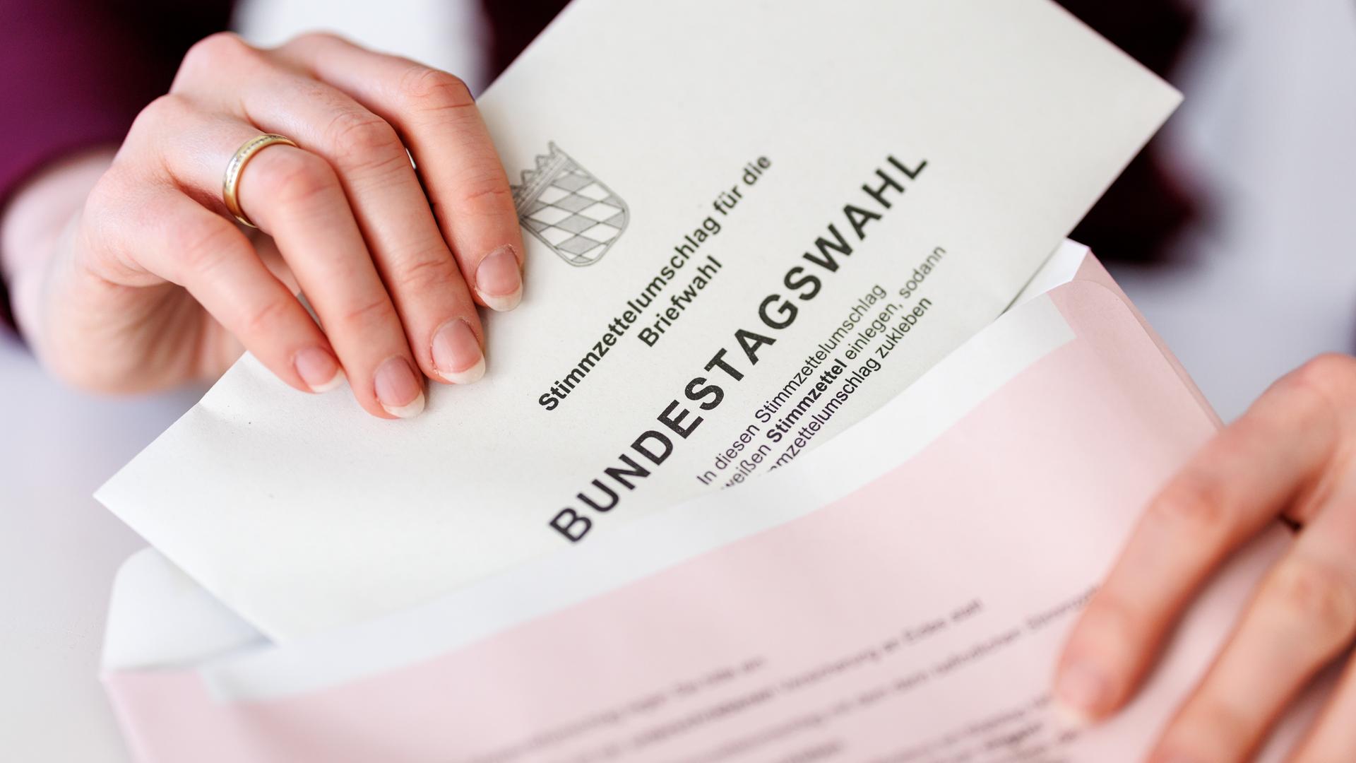 Eine Frau steckt in München (Bayern) einen Stimmzettelumschlag für die Briefwahl zur Bundestagswahl 2025 in den roten Wahlbriefumschlag.