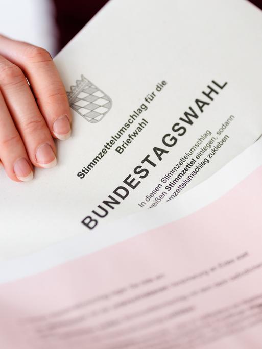 Eine Frau steckt in München (Bayern) einen Stimmzettelumschlag für die Briefwahl zur Bundestagswahl 2025 in den roten Wahlbriefumschlag.