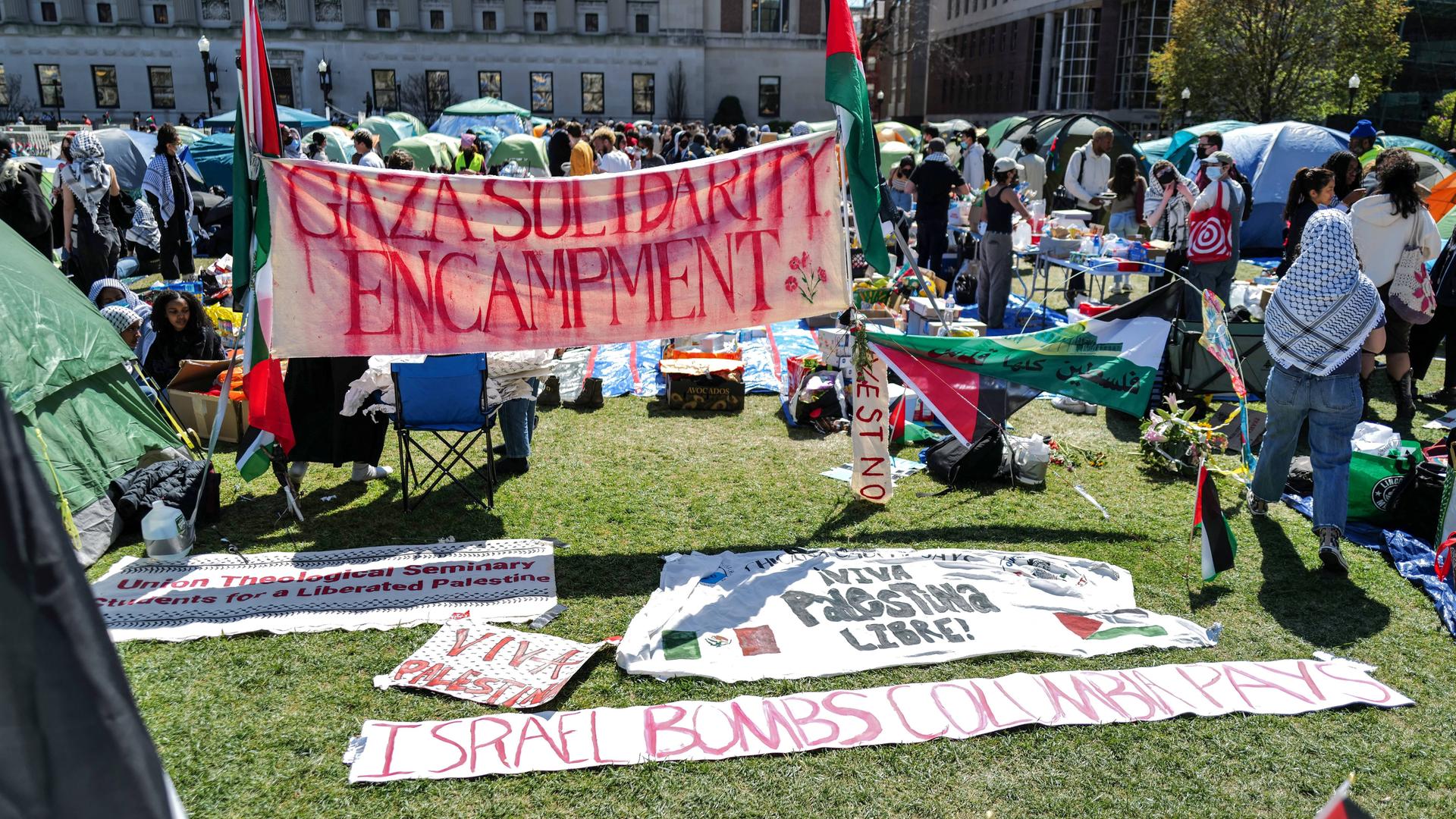 Auf einem Rasen liegen Plakate, Demonstranten haben Zelte aufgestellt.