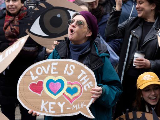 Eine Protestierende steht zwischen Menschen, ruft und hält ein Schild, auf dem steht: "Love is the key".