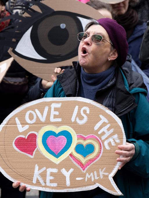 Eine Protestierende steht zwischen Menschen, ruft und hält ein Schild, auf dem steht: "Love is the key".