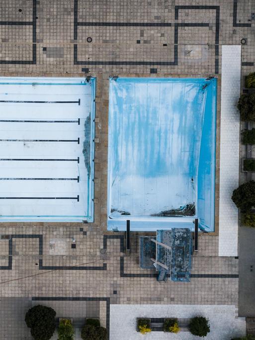 Vogelperspektive auf ein leeres Freibad mit abgelassenen Schwimmbecken.