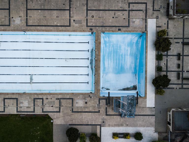 Vogelperspektive auf ein leeres Freibad mit abgelassenen Schwimmbecken.