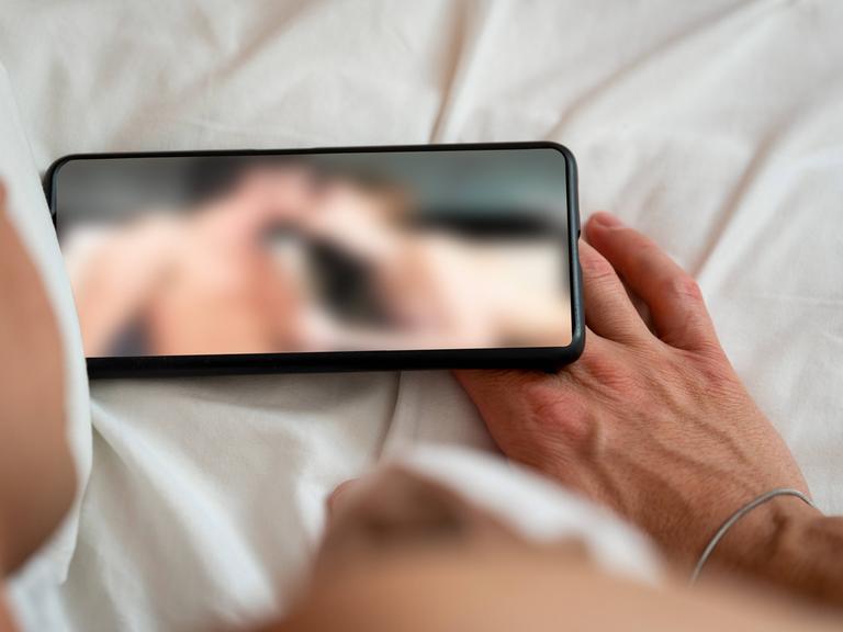 Eine Person schaut sich auf einem Smartphone eine Porno-Internetseite an