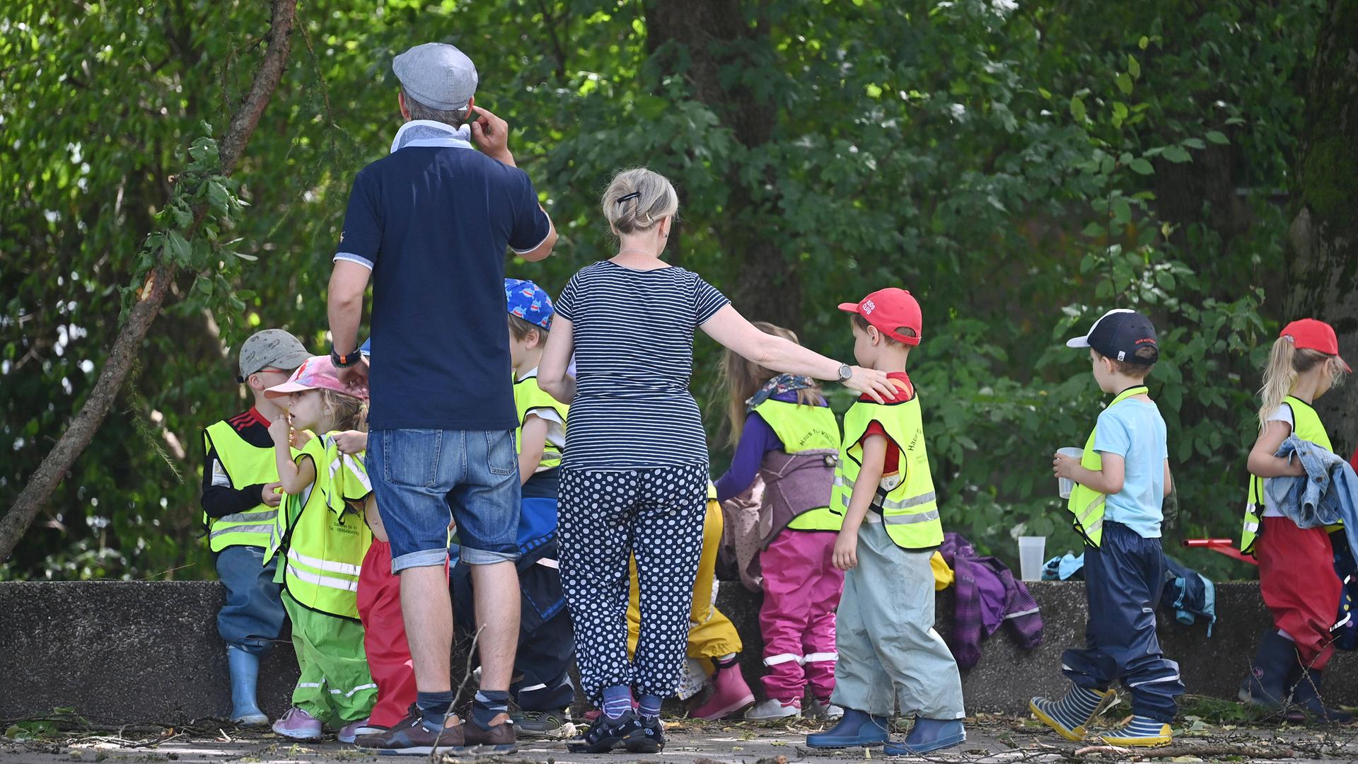 Kindergartenkinder mit Betreuer und Betreuerin machen eine Wanderung, die Kinder tragen gelbe Warnwesten.