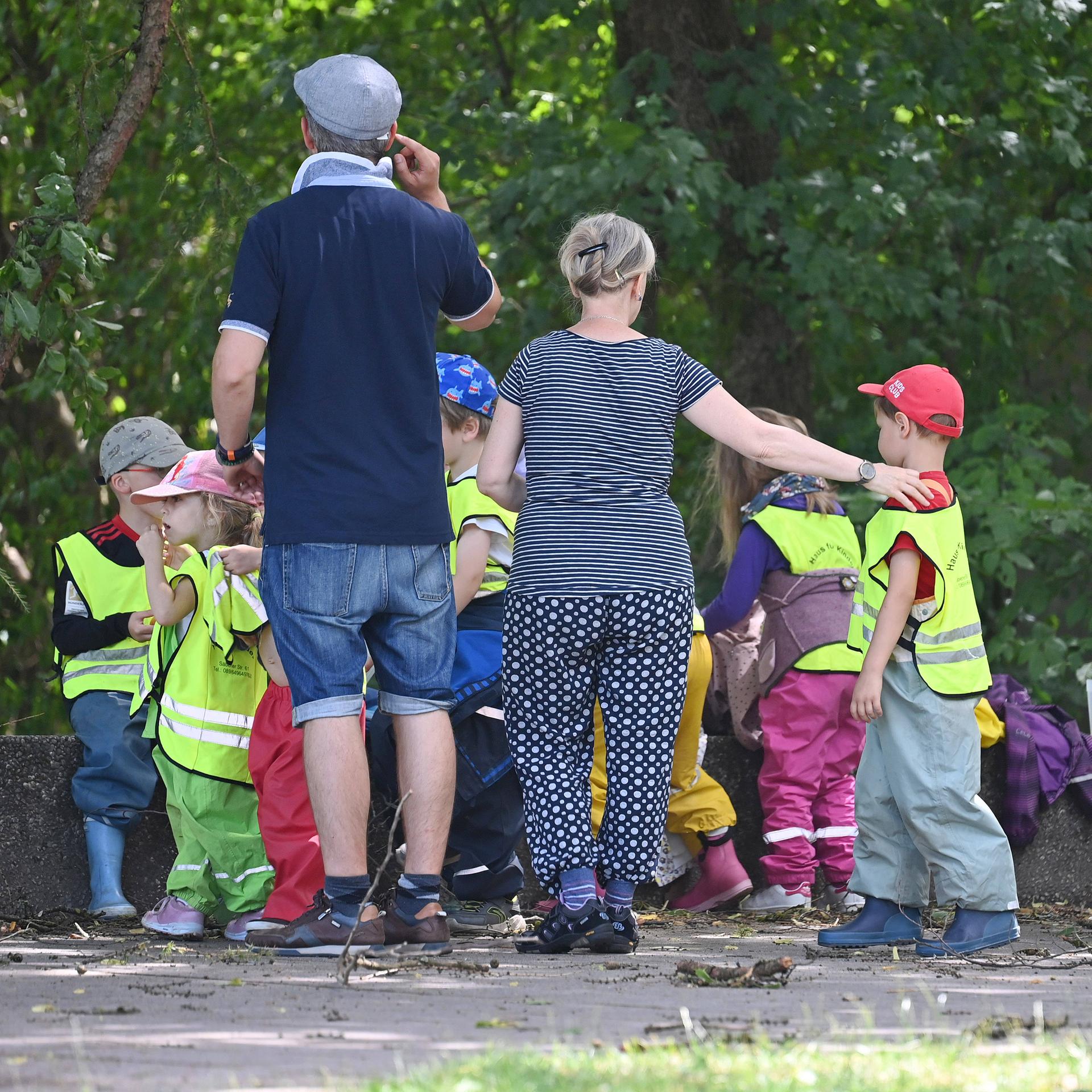 Kindergartenkinder mit Betreuer und Betreuerin machen eine Wanderung, die Kinder tragen gelbe Warnwesten.