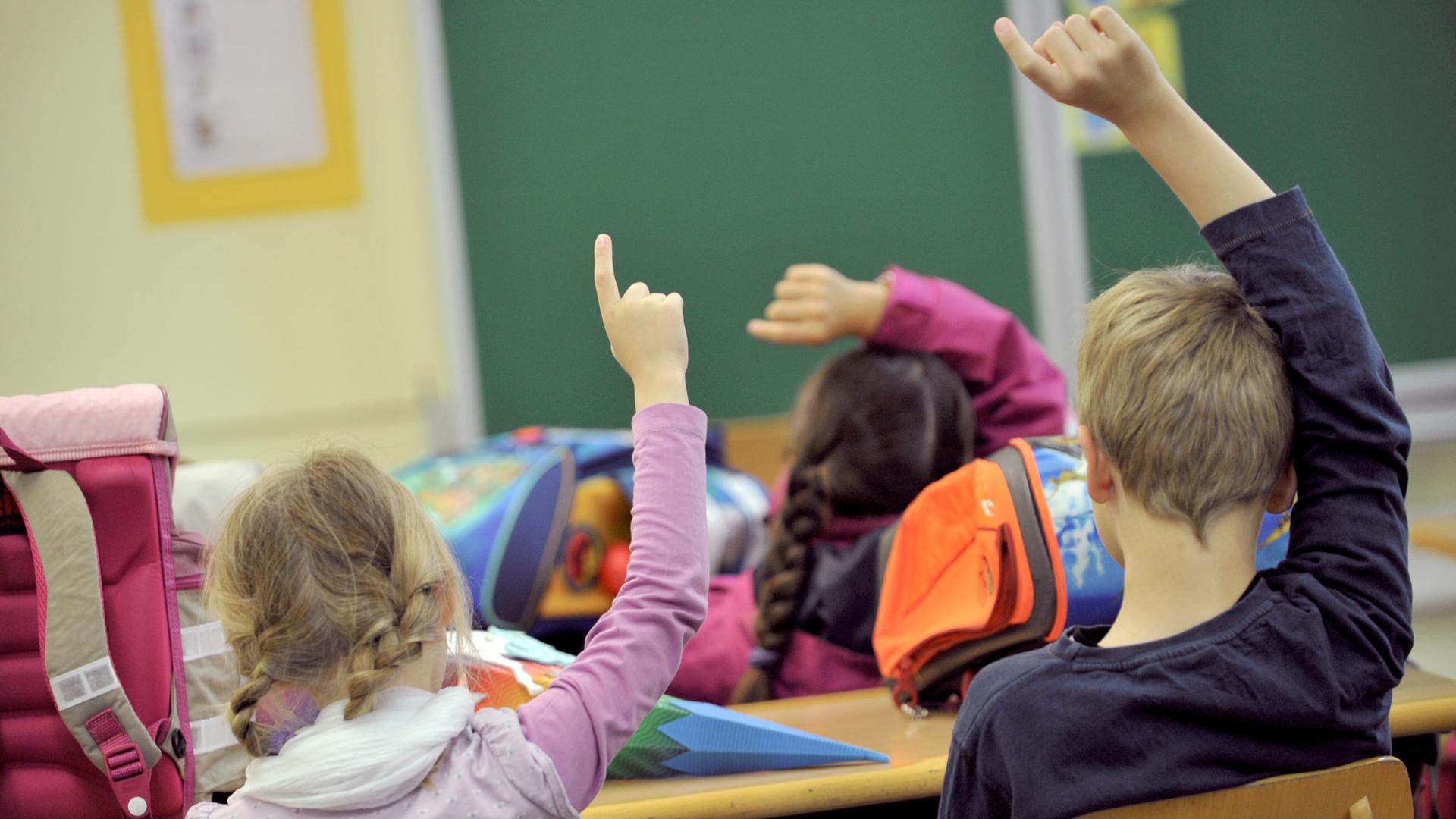 Kinder melden sich beim Unterricht in einer Grundschule. Sie wurden von hinten fotografiert.