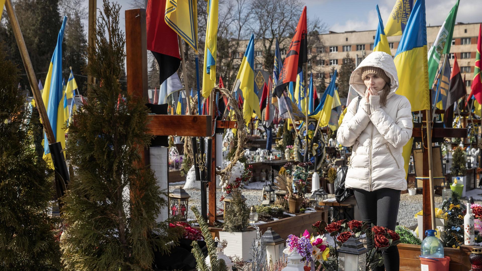 Eine Frau trauert auf einem Friedhof in Lwiw, um sie herum Gräber und blaue gelbe Flaggen.