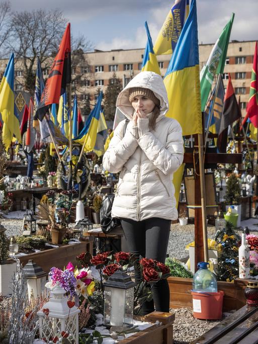 Eine Frau trauert auf einem Friedhof in Lwiw, um sie herum Gräber und blaue gelbe Flaggen.