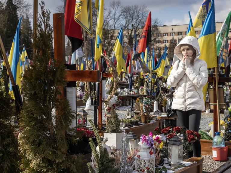 Eine Frau trauert auf einem Friedhof in Lwiw, um sie herum Gräber und blaue gelbe Flaggen.