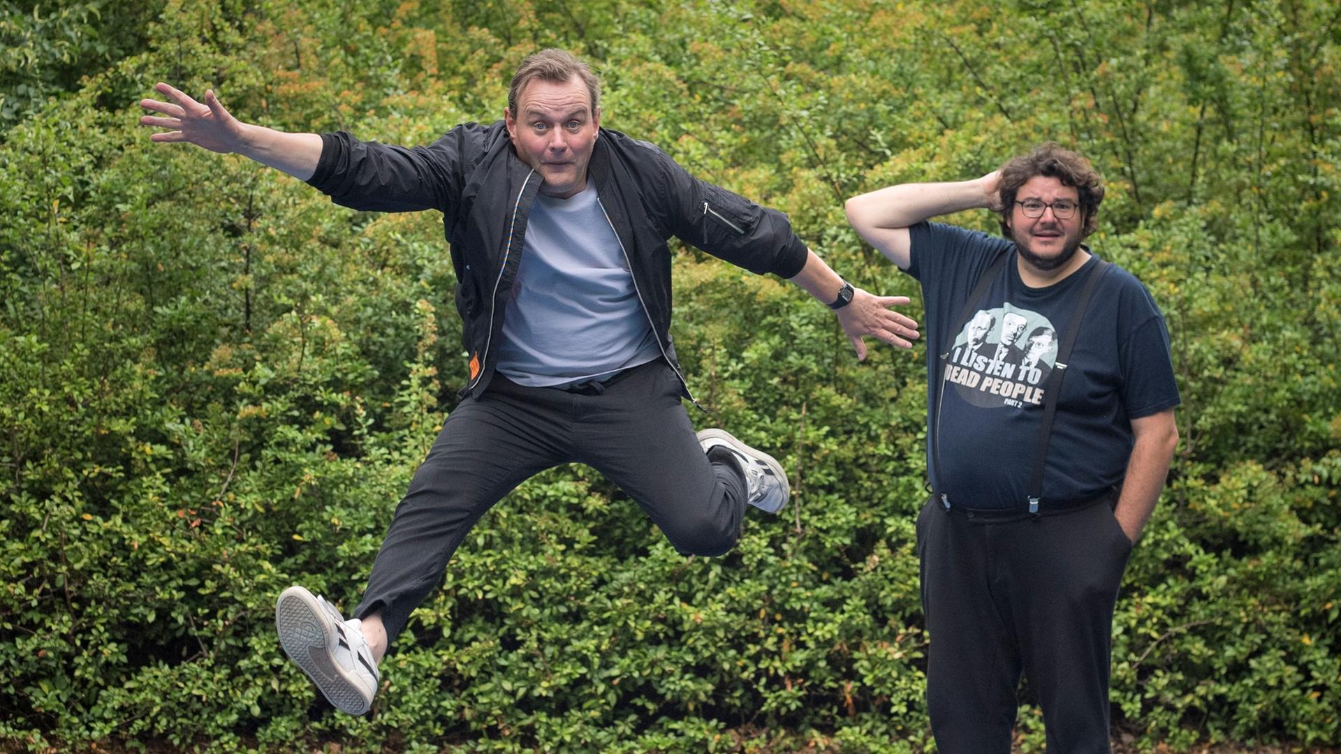 Devid Striesow und Axel Ranisch stehen auf einem Spielplatz mit Bodentrampolin. Devid Striesow springt in die Luft. Devid Striesow und Axel Ranisch stehen auf einem Spielplatz mit Bodentrampolin. Devid Striesow springt in die Luft.