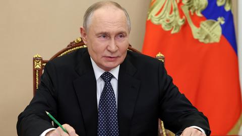 Russlands Präsident Wladimir Putin sitzt bei einem Treffen an einem Tisch, beide Unterarme aufgestützt, in der linken Hand einen Bleistift mit der Spitze nach oben.