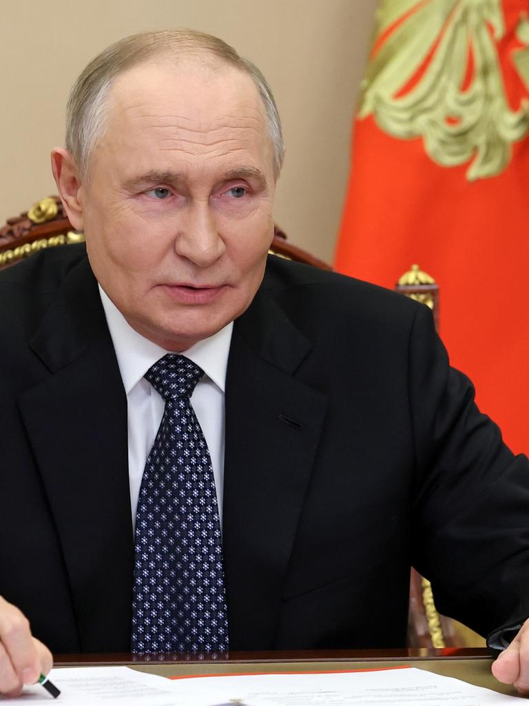 Russlands Präsident Wladimir Putin sitzt bei einem Treffen an einem Tisch, beide Unterarme aufgestützt, in der linken Hand einen Bleistift mit der Spitze nach oben.