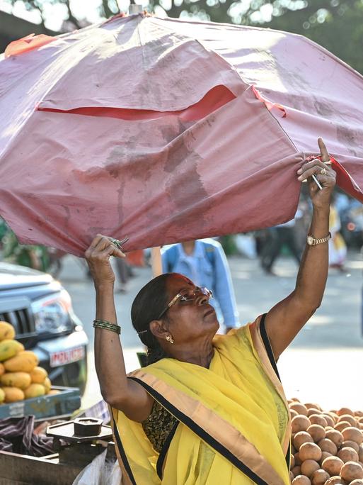 Eine Obstverkäuferin spannt einen Sonnenschirm über ihren Waren auf.