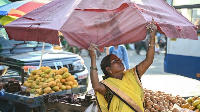 Eine Obstverkäuferin spannt einen Sonnenschirm über ihren Waren auf.