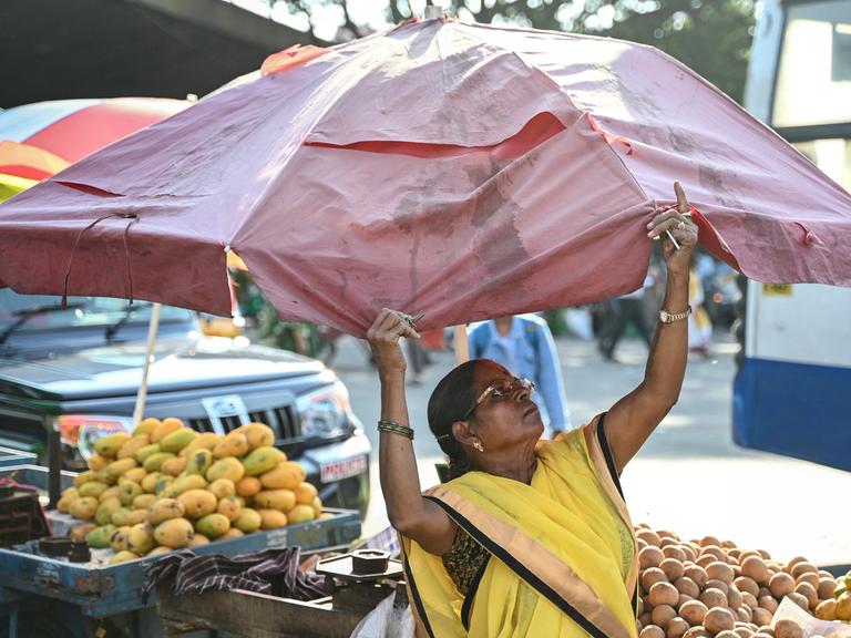 Eine Obstverkäuferin spannt einen Sonnenschirm über ihren Waren auf.