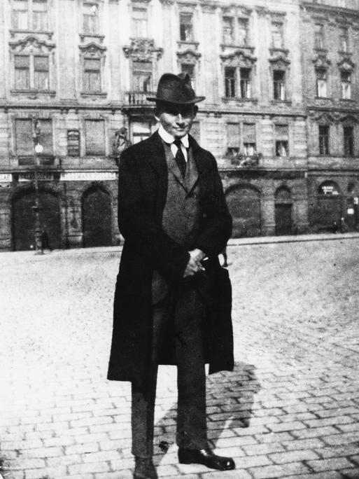 Schwarz-weiß-Foto Franz Kafkas. Der Autor trägt einen Hut, er steht auf einem Platz.