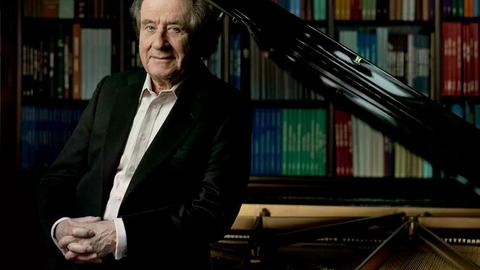 Rudolf Buchbinder steht an seinem heimischen Flügel, hinter dem Regale voller Noten zu erkennen sind. Rudolf Buchbinder steht an seinem heimischen Flügel, hinter dem Regale voller Noten zu erkennen sind.