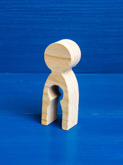 Symboldbild für den Verlust einer Schwangerschaft/eines Kindes: Eine Holzfigur hat in ihrem Unterleib eine Auslassung in Form einer kleinen Figur.