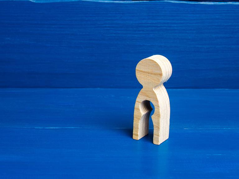 Symboldbild für den Verlust einer Schwangerschaft/eines Kindes: Eine Holzfigur hat in ihrem Unterleib eine Auslassung in Form einer kleinen Figur.