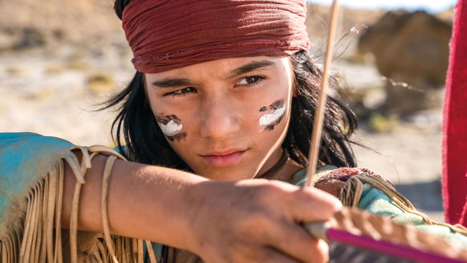Ein Junge in einem Winnetou-Kostüm schießt mit Pfeil und Bogen.