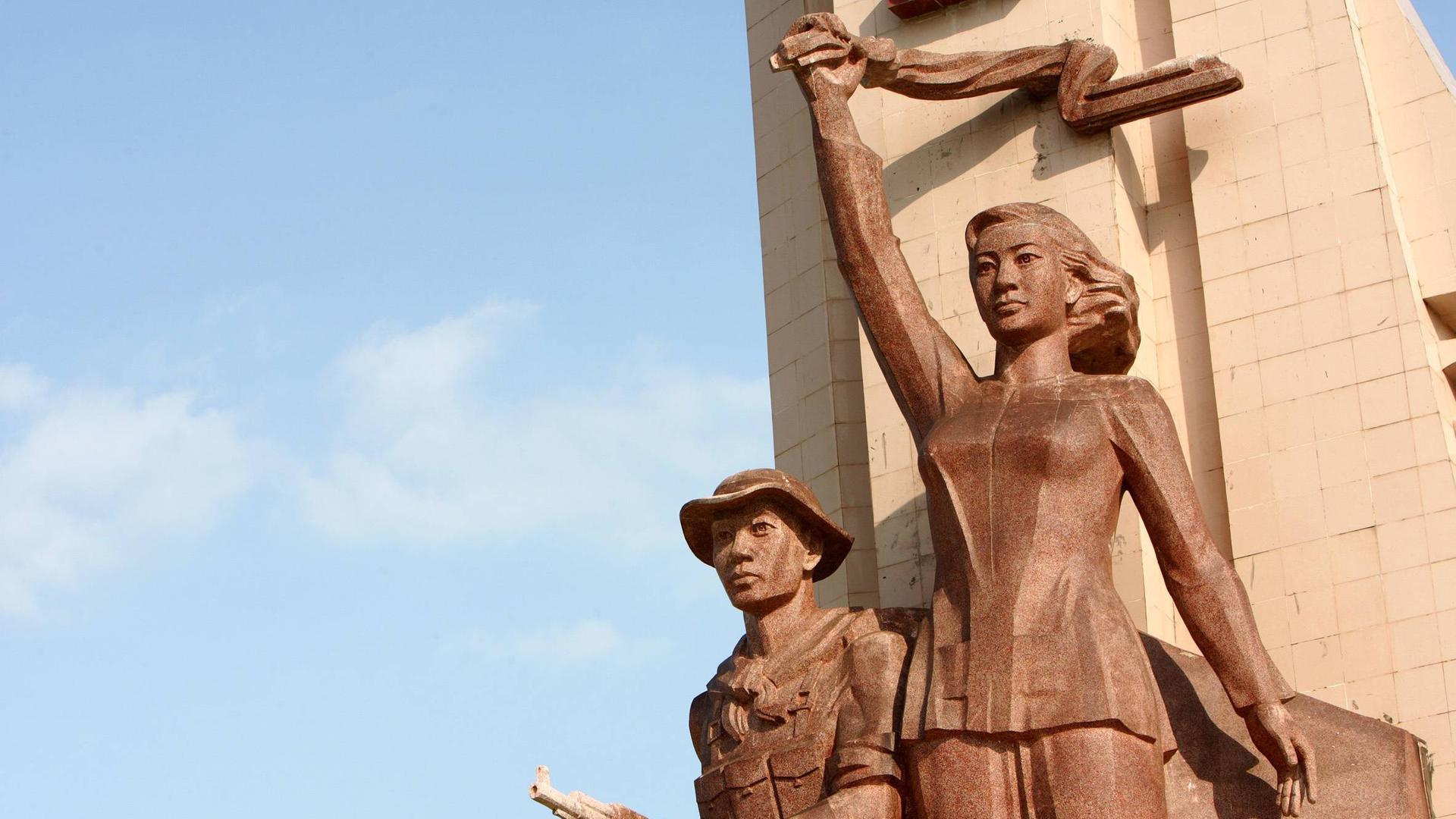 Ein vietnamesisches Märtyrerdenkmal auf einem Heldenfriedhof für die vietnamesischen Gefallenen des Vietnamkrieges in Can Tho. Die Statue einer Frau hält ein Tuch über ihrem Kopf. Darunter die Statue eines Mannes in Soldaten-Uniform mit Hut und Waffe.