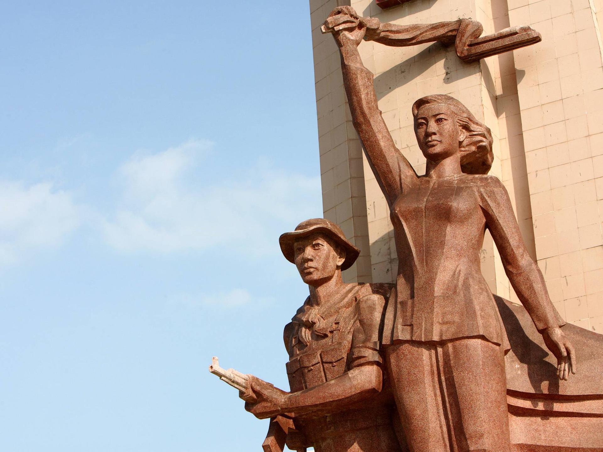 Ein vietnamesisches Märtyrerdenkmal auf einem Heldenfriedhof für die vietnamesischen Gefallenen des Vietnamkrieges in Can Tho. Die Statue einer Frau hält ein Tuch über ihrem Kopf. Darunter die Statue eines Mannes in Soldaten-Uniform mit Hut und Waffe.