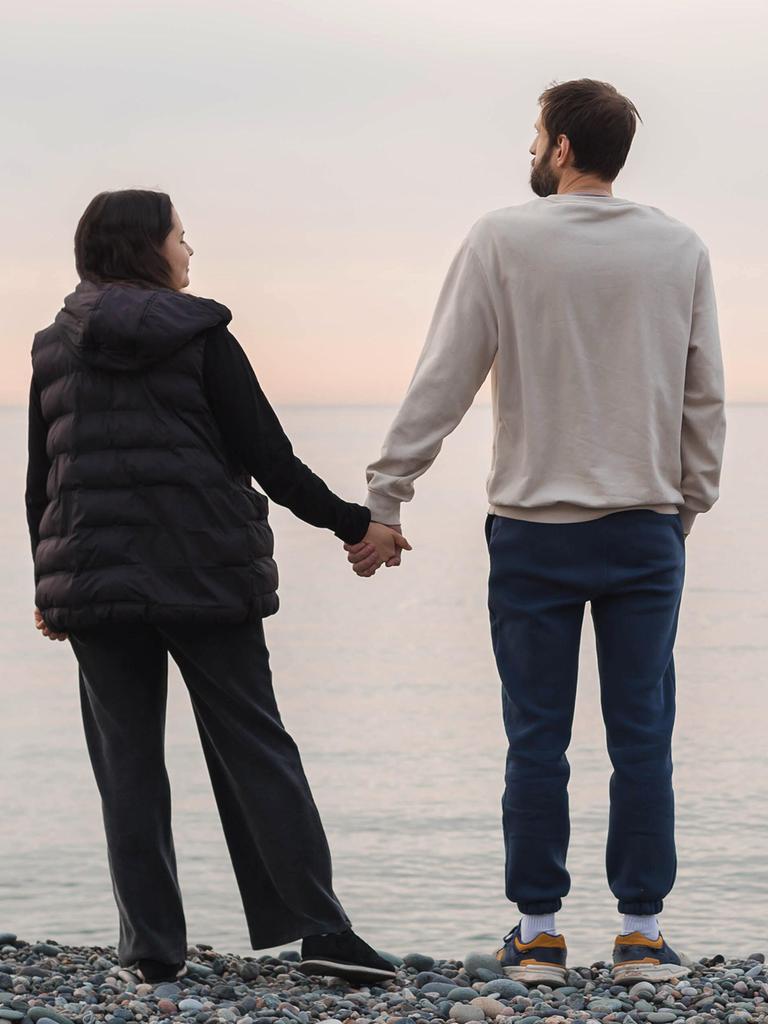 Ein Paar steht an einem Strand und hält sich an den Händen beim Blick aufs Meer (Symbolfoto). Ein Paar steht an einem Strand und hält sich an den Händen beim Blick aufs Meer (Symbolfoto).