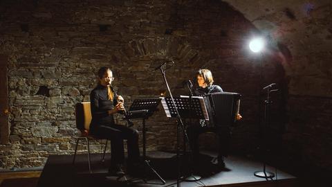 Auf dem Podium eines Konzertkellers sitzen zwei Instrumentalistinnen mit Klarinette und Akkordeon im Scheinwerferlicht