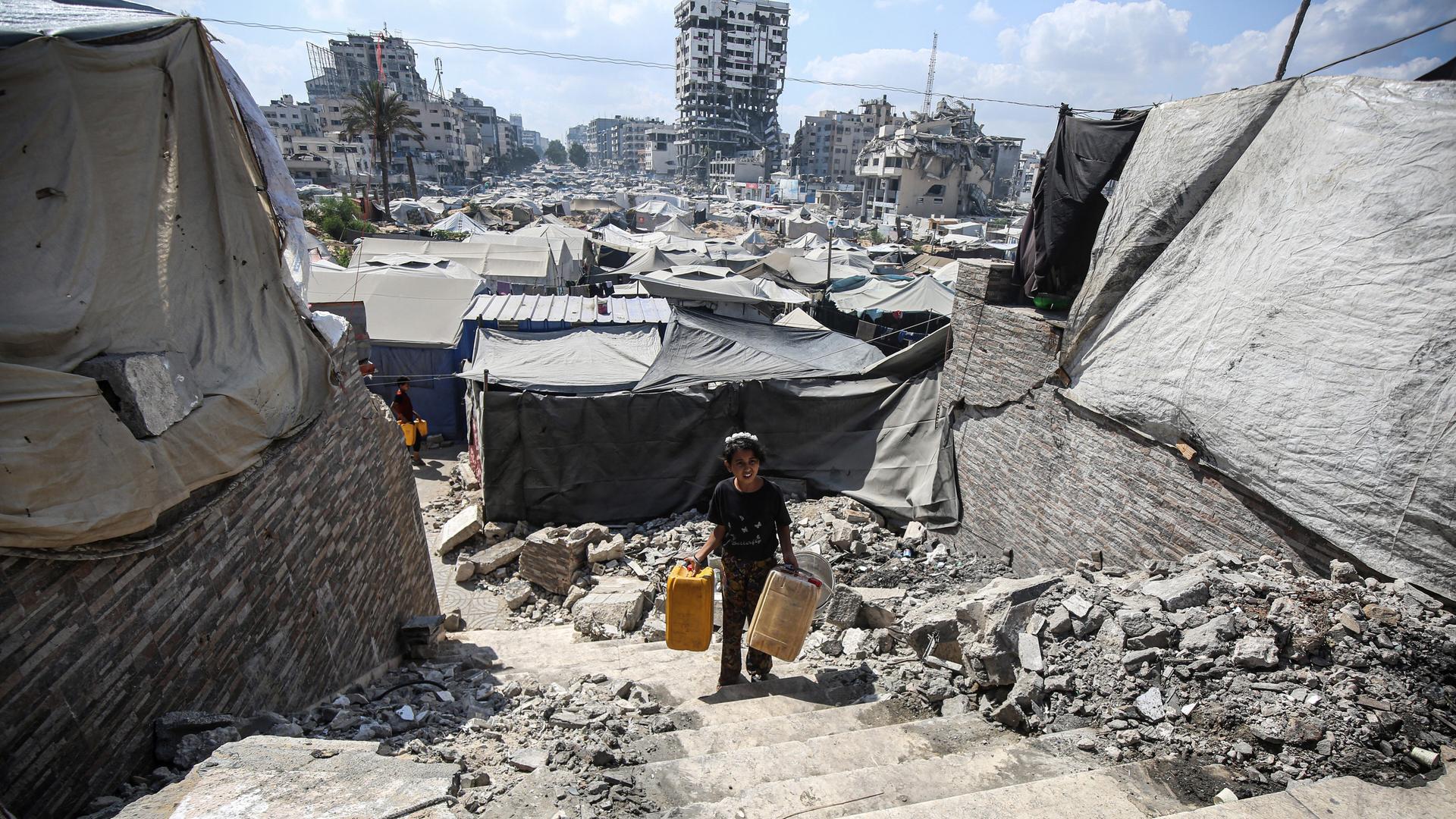 Ein Junge läuft mit Eimern für Wasser durch zerstörte Gebäude in Gaza-Stadt.