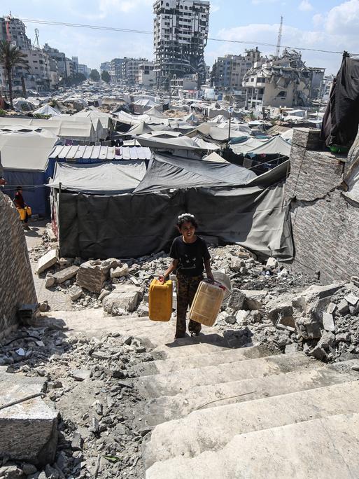 Ein Junge läuft mit Eimern für Wasser durch zerstörte Gebäude in Gaza-Stadt.