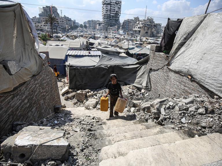 Ein Junge läuft mit Eimern für Wasser durch zerstörte Gebäude in Gaza-Stadt.